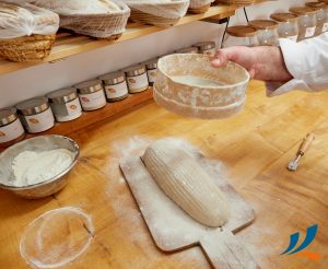 Verarbeitung von Getreide. Ein ungebackenes Brot liegt auf einem Brett und wird mit Mehl bestäubt.
