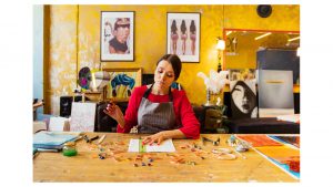Kunsthandwerk: eine Frau sitzt am Schreibtisch und stellt Schmuck her