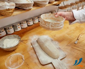 Verarbeitung von Getreide. Ein ungebackenes Brot liegt auf einem Brett und wird mit Mehl bestäubt.